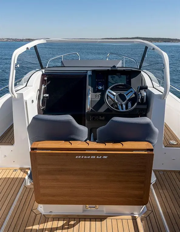 Stylish boat cockpit featuring upholstered seats, steering wheel, and digital display against a backdrop of calm water.